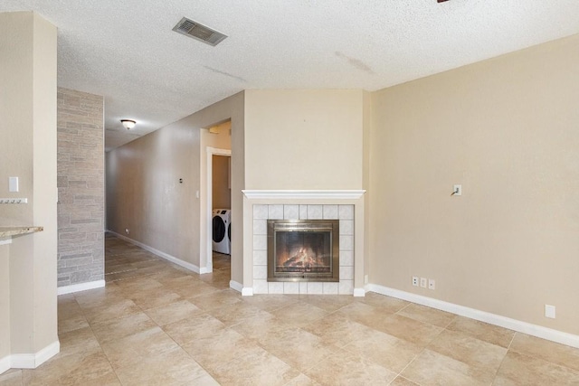 unfurnished living room with a tile fireplace, washer / dryer, and a textured ceiling