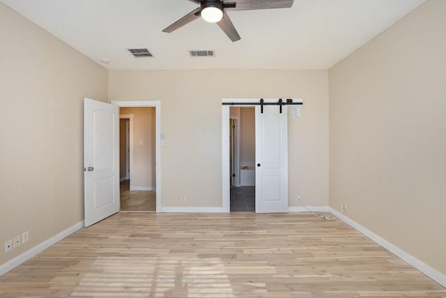 unfurnished bedroom with ceiling fan, a barn door, and light hardwood / wood-style flooring