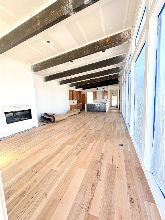 unfurnished living room featuring heating unit, light hardwood / wood-style flooring, and beamed ceiling