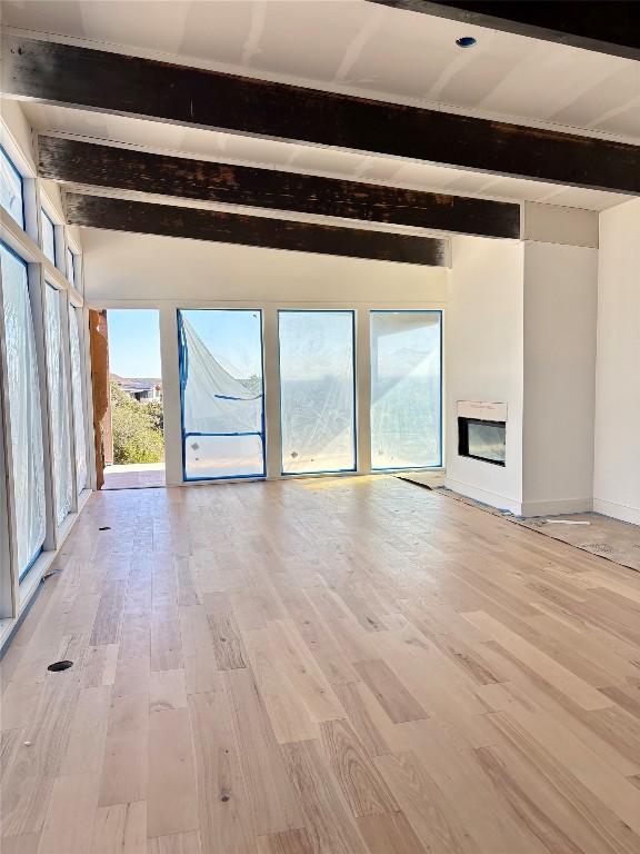 unfurnished living room with beam ceiling and light wood-type flooring