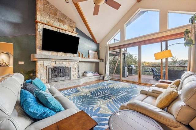 living room with beamed ceiling, ceiling fan, a stone fireplace, and high vaulted ceiling