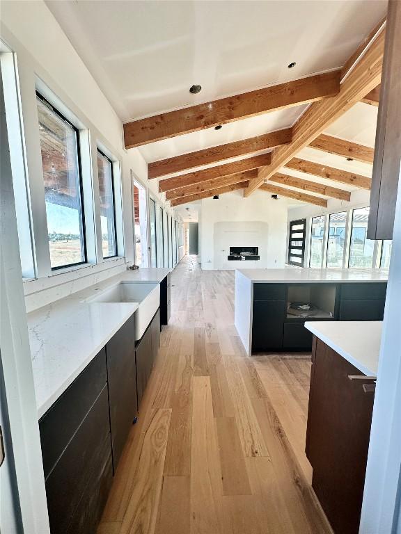 kitchen featuring a fireplace, light hardwood / wood-style flooring, and lofted ceiling with beams