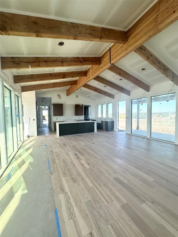 unfurnished living room featuring lofted ceiling with beams and light wood-type flooring