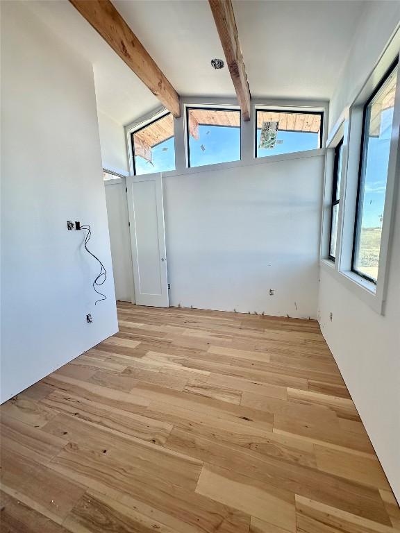 empty room with vaulted ceiling with beams and light wood-type flooring