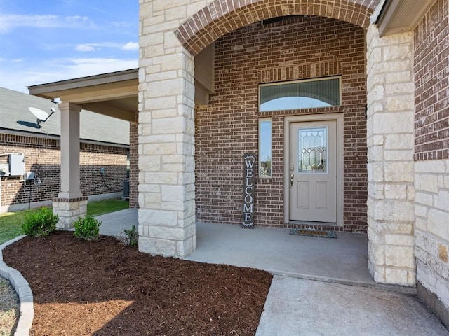 view of exterior entry with a porch, brick siding, and central air condition unit