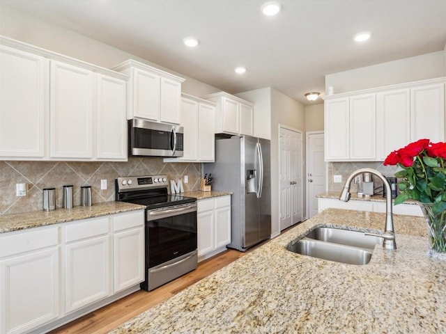 kitchen with decorative backsplash, appliances with stainless steel finishes, light wood-type flooring, sink, and white cabinetry