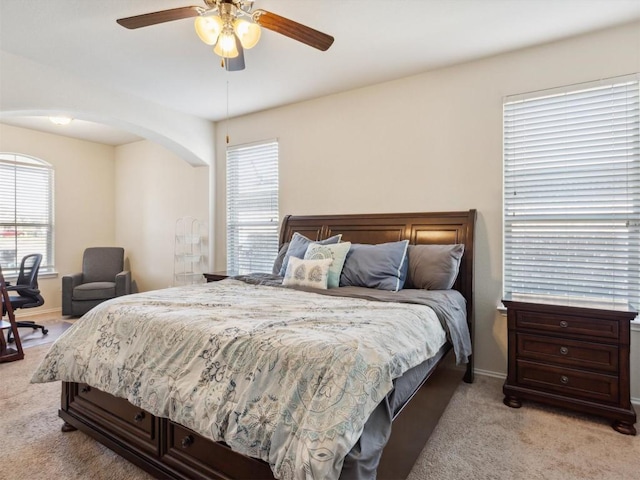 bedroom featuring light carpet, arched walkways, a ceiling fan, and baseboards