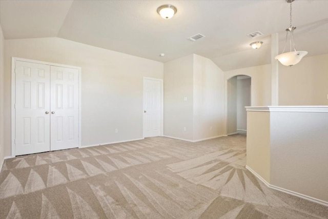 empty room featuring arched walkways, vaulted ceiling, visible vents, and light colored carpet