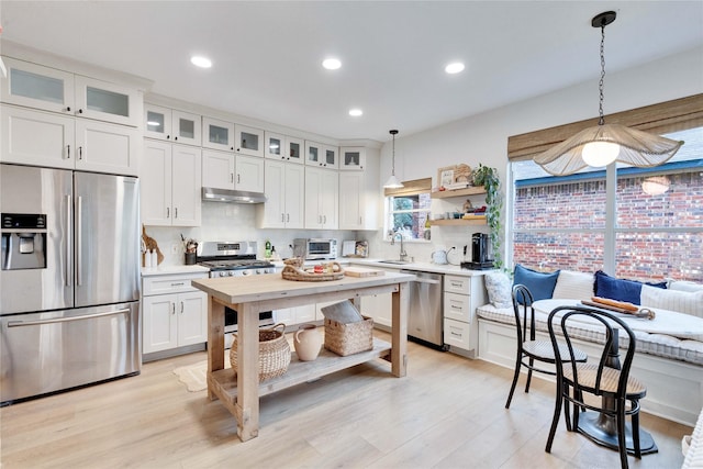 kitchen with decorative backsplash, hanging light fixtures, light wood-type flooring, stainless steel appliances, and white cabinets