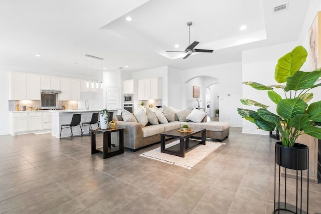 living room with a tray ceiling, ceiling fan, sink, and light tile patterned floors