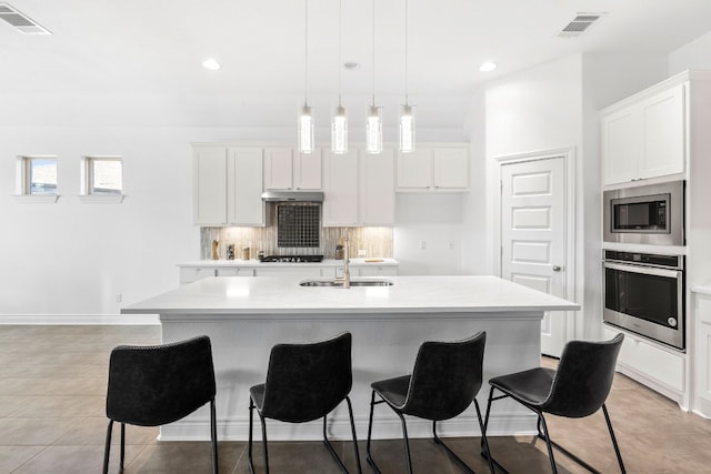 kitchen with pendant lighting, a kitchen island with sink, sink, appliances with stainless steel finishes, and white cabinetry