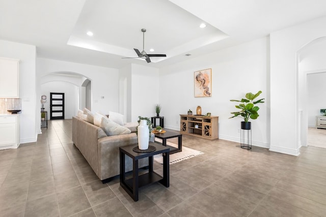 living room with ceiling fan, light tile patterned flooring, and a tray ceiling