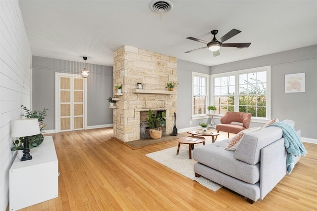 living room with a stone fireplace, ceiling fan, and light hardwood / wood-style flooring