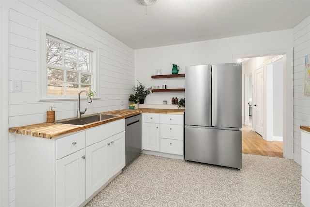 kitchen featuring appliances with stainless steel finishes, wooden walls, sink, white cabinets, and butcher block countertops