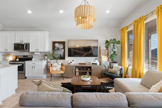 living area with light wood-type flooring, vaulted ceiling, a notable chandelier, and recessed lighting