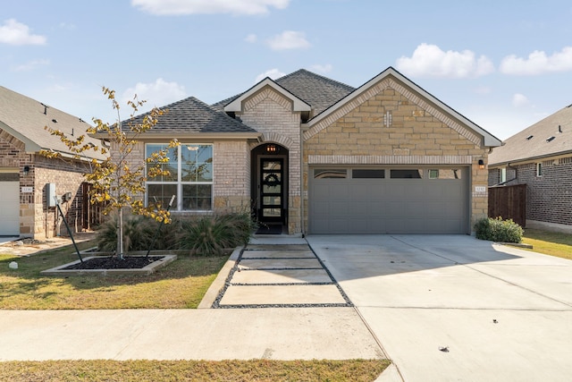 view of front of property featuring brick siding, roof with shingles, an attached garage, stone siding, and driveway