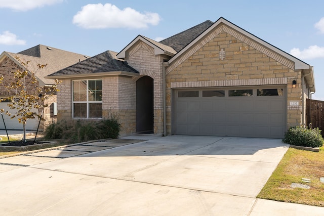 view of front facade featuring concrete driveway, stone siding, roof with shingles, an attached garage, and brick siding