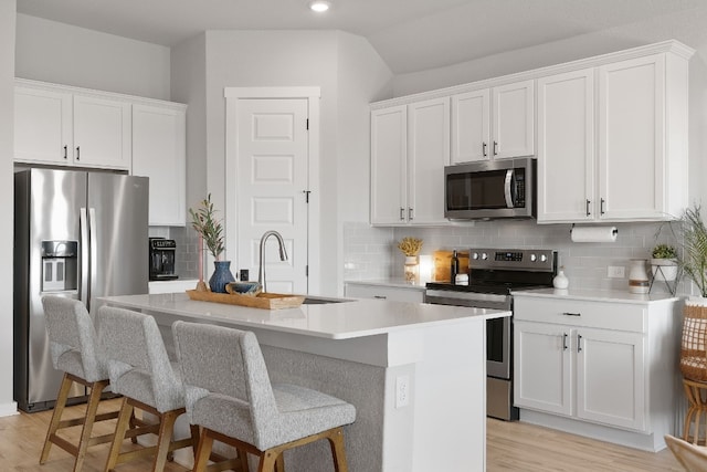 kitchen with stainless steel appliances, light countertops, a kitchen island with sink, and backsplash