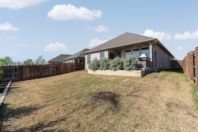 back of house with a fenced backyard, a lawn, and brick siding