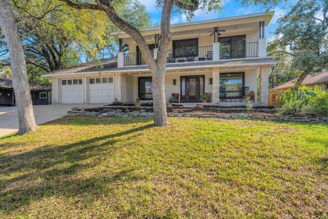 view of front facade with a balcony, a front lawn, ceiling fan, covered porch, and a garage