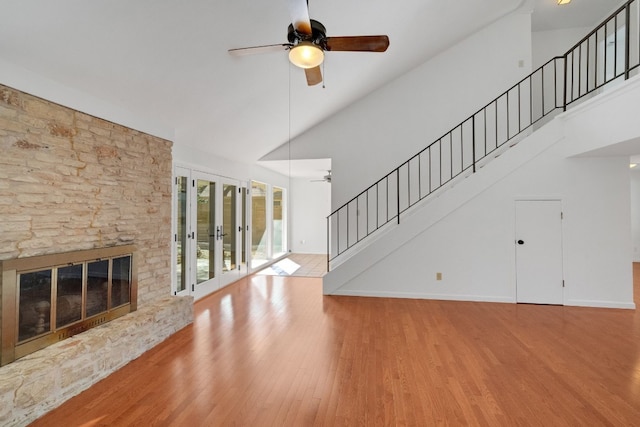 unfurnished living room with high vaulted ceiling, french doors, a stone fireplace, light hardwood / wood-style flooring, and ceiling fan