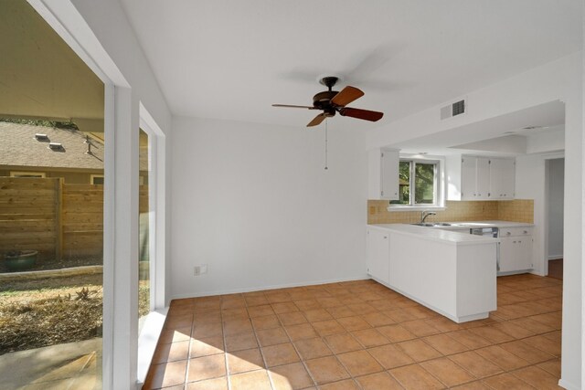 kitchen with sink, light tile patterned floors, tasteful backsplash, kitchen peninsula, and white cabinets