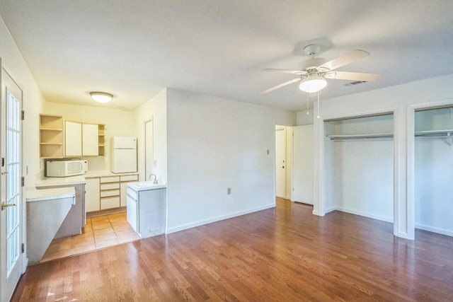 unfurnished bedroom featuring two closets, sink, light hardwood / wood-style flooring, ceiling fan, and white fridge