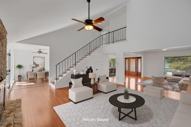 living room featuring ceiling fan, light hardwood / wood-style floors, and a towering ceiling