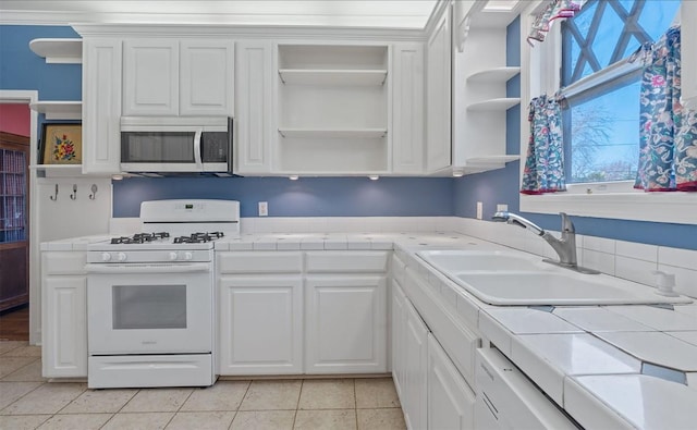 kitchen featuring white gas range, tile counters, white cabinets, and sink