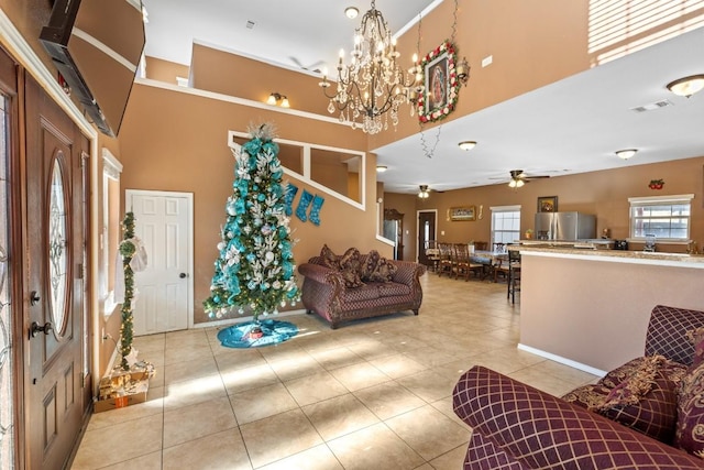 tiled living room featuring ceiling fan with notable chandelier and a high ceiling