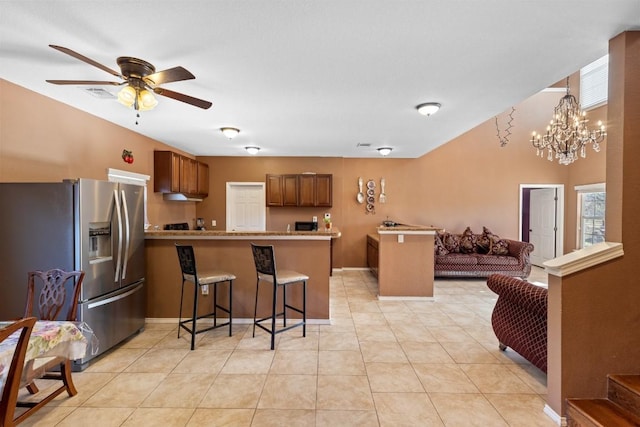 kitchen featuring stainless steel refrigerator with ice dispenser, kitchen peninsula, a kitchen bar, light tile patterned floors, and ceiling fan with notable chandelier