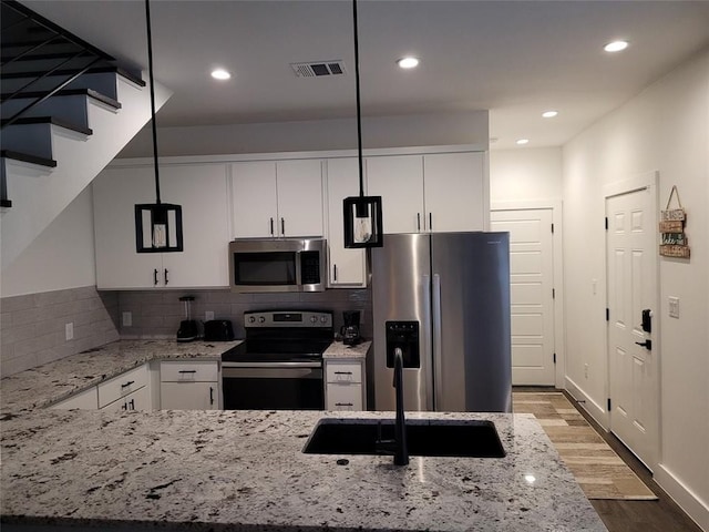 kitchen featuring sink, light stone counters, decorative light fixtures, white cabinets, and appliances with stainless steel finishes