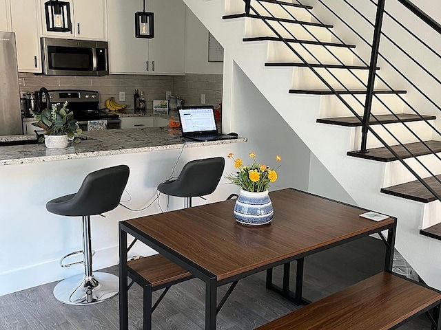 kitchen featuring white cabinets, dark hardwood / wood-style floors, light stone countertops, tasteful backsplash, and stainless steel appliances