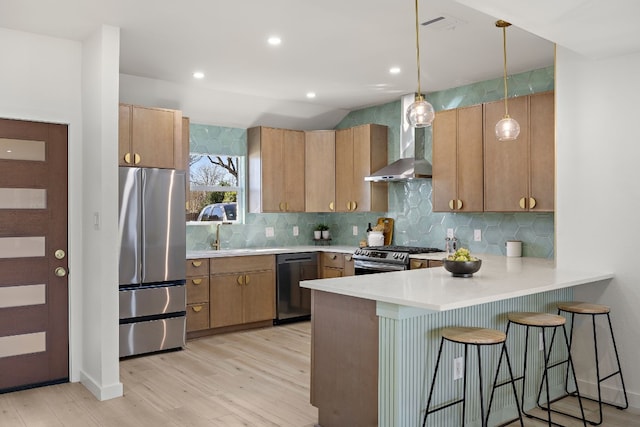 kitchen featuring pendant lighting, wall chimney range hood, light hardwood / wood-style flooring, a kitchen bar, and stainless steel appliances