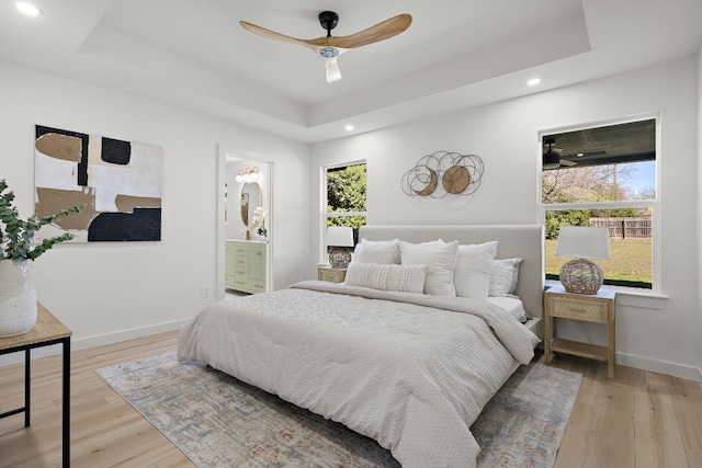 bedroom with a raised ceiling, ensuite bathroom, and light wood-type flooring