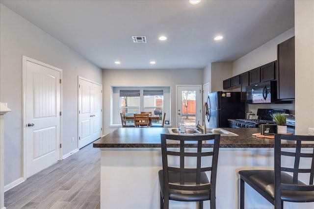 kitchen featuring sink, a kitchen breakfast bar, kitchen peninsula, light hardwood / wood-style floors, and black appliances