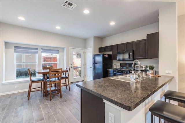 kitchen with kitchen peninsula, a kitchen breakfast bar, dark brown cabinetry, sink, and black appliances