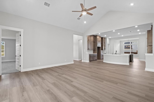 unfurnished living room with ceiling fan, sink, high vaulted ceiling, and light hardwood / wood-style floors