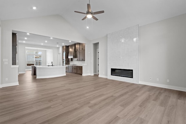 unfurnished living room with ceiling fan, a large fireplace, light wood-type flooring, and sink