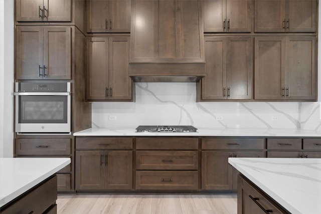 kitchen with decorative backsplash, dark brown cabinets, light stone countertops, and stainless steel appliances