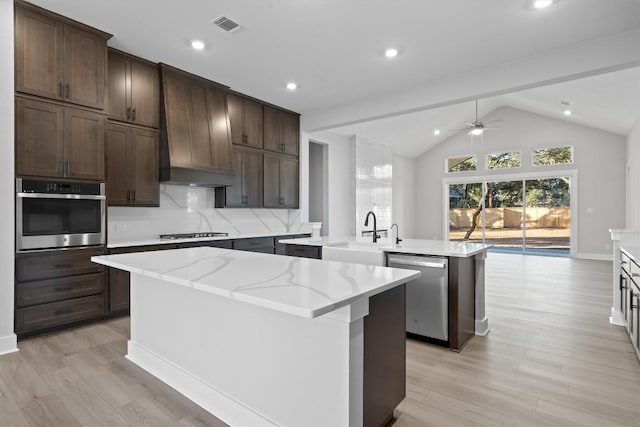 kitchen with sink, stainless steel appliances, light stone counters, lofted ceiling, and a kitchen island with sink