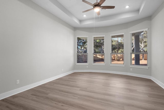 spare room with a raised ceiling, ceiling fan, and light hardwood / wood-style flooring