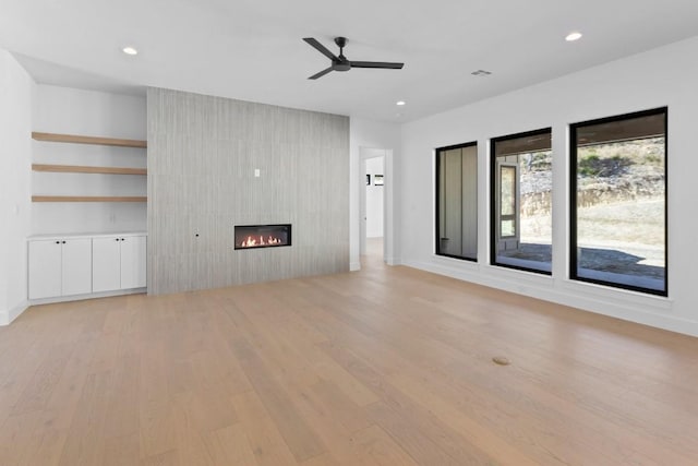 unfurnished living room with ceiling fan, a large fireplace, and light hardwood / wood-style floors