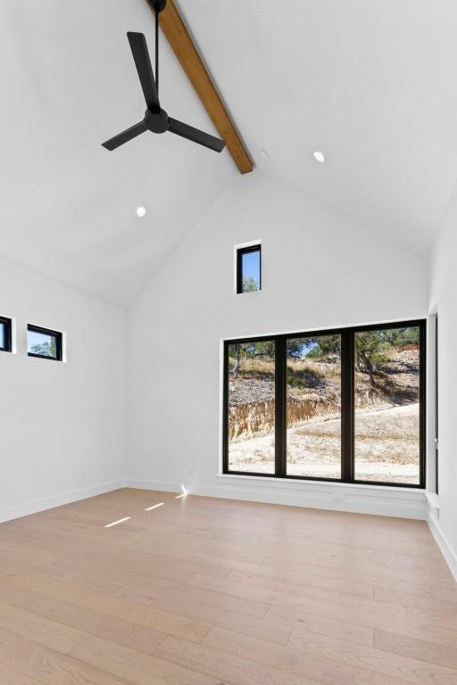 unfurnished living room with ceiling fan, beamed ceiling, high vaulted ceiling, and light wood-type flooring