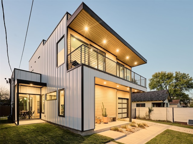 back house at dusk with a balcony and a lawn