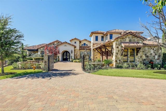 mediterranean / spanish-style home featuring stone siding, a tiled roof, decorative driveway, stucco siding, and a front yard