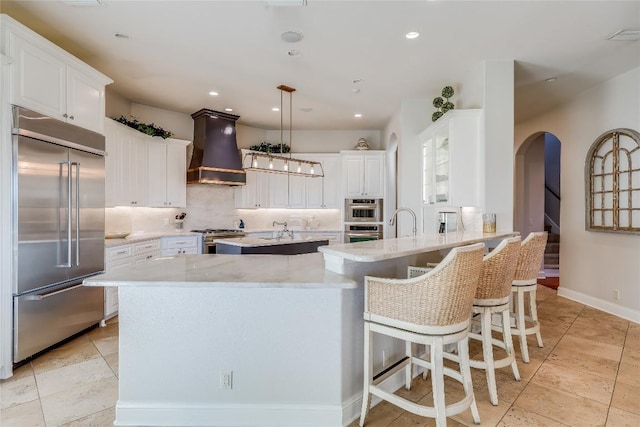 403 Rough Hollow Cv, Austin, TX 78734 - kitchen with high end appliances, custom exhaust hood, a center island with sink, a peninsula, and arched walkways