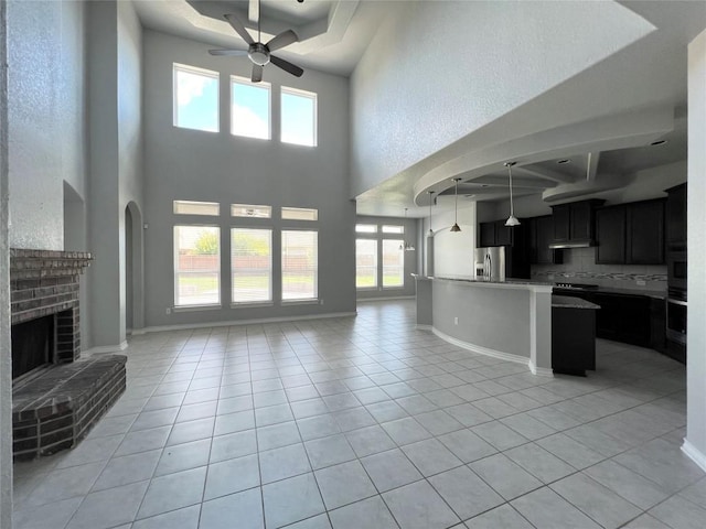 unfurnished living room featuring light tile patterned floors, a brick fireplace, ceiling fan, and a healthy amount of sunlight