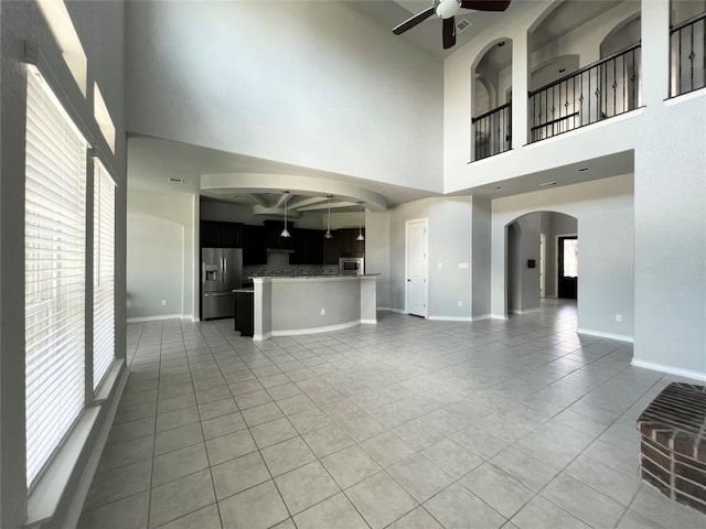 unfurnished living room with beamed ceiling, ceiling fan, plenty of natural light, and light tile patterned floors