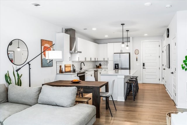 kitchen with white cabinetry, stainless steel appliances, wall chimney range hood, pendant lighting, and decorative backsplash